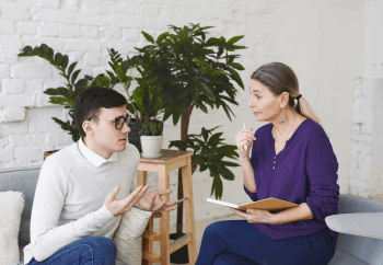 service-4-1 Psychology, therapy, psychiatry, mental health and counseling concept. Candid shot of nervous self conscious young male in glasses telling middle aged female counselor about his problems at work